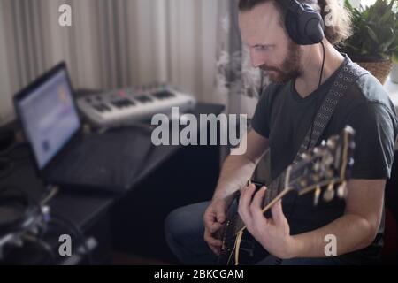 Bärtiger Mann Musiker Musik spielen und komponieren ein Lied mit E-Gitarre Klavier und Laptop-Computer, während im Wohnzimmer sitzen, Corona Virus quar Stockfoto