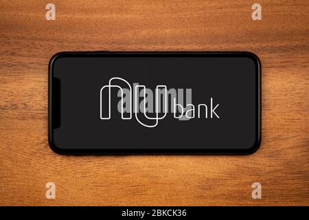 Ein Smartphone mit dem Logo der Nu Bank liegt auf einem einfachen Holztisch (nur für redaktionelle Zwecke). Stockfoto