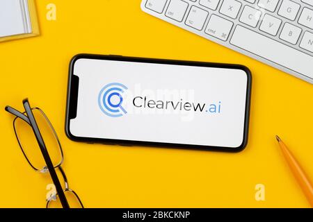 Ein Smartphone mit dem Clearview.ai Logo liegt auf einem gelben Hintergrund zusammen mit Tastatur, Brille, Stift und Buch (nur für redaktionelle Verwendung). Stockfoto