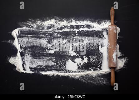 Weißes Weizenmehl auf einem schwarzen Tisch und einem hölzernen Nudelholz auf einem schwarzen Tisch verstreut, Draufsicht, Platz für eine Inschrift Stockfoto