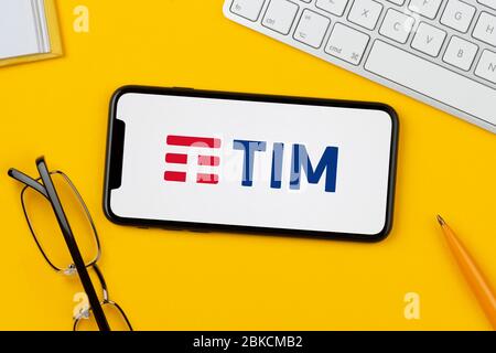 Ein Smartphone mit dem Logo von Telecom Italia (Tim) liegt auf einem gelben Hintergrund zusammen mit Tastatur, Brille, Stift und Buch (nur für redaktionelle Zwecke). Stockfoto