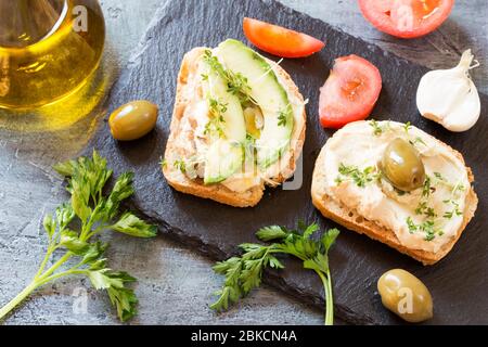 Hummus Sandwiches mit Avocado und Micro Rucola Sprößlinge auf schwarzem Granit board Stockfoto