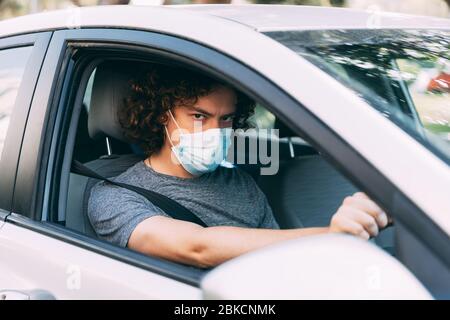 Ein Mann fährt ein Auto in einer medizinischen Maske. Ein Mann in einer Schutzmaske sitzt hinter dem Lenkrad eines Autos. Taxifahrer in Maske. Schutz vor Coronavirus-epid Stockfoto