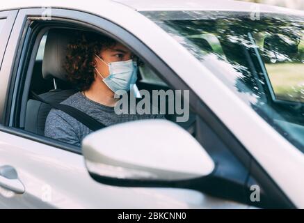 Ein Mann fährt ein Auto in einer medizinischen Maske. Ein Mann in einer Schutzmaske sitzt hinter dem Lenkrad eines Autos. Taxifahrer in Maske. Schutz vor Coronavirus-epid Stockfoto