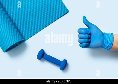 Training zu Hause - Schützen Sie sich und andere vor Krankheiten. Die Hand einer Frau in einem medizinischen Gander hält eine Hantel. Stockfoto