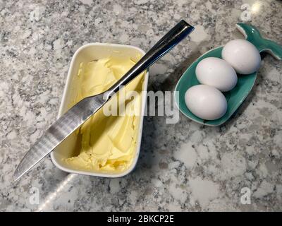 Eier in einem Wallöffel ruhen und eine Wanne Butter mit einem Messer darauf warten gebraten werden. Stockfoto