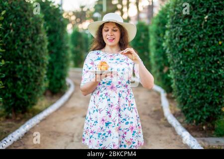 Ziemlich lustige Frau, die den Kuchen im Park isst. Essen, Ernährung, ungesunde Lebensmittel und süße Konzept. Zuckersucht. Stockfoto