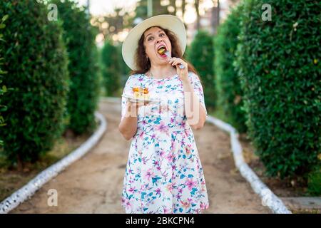 Ziemlich lustige Frau, die den Kuchen im Park isst. Essen, Ernährung, ungesunde Lebensmittel und süße Konzept. Zuckersucht. Stockfoto