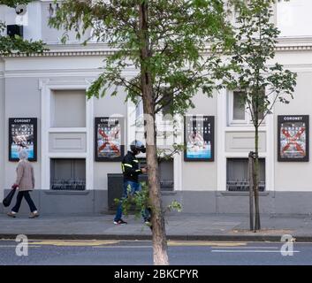 Zwei Personen gehen am Coronet Theater vorbei und zeigen Plakate für Produktionen ein weiterer Blick auf Erinnerung und Jugend ohne Gott, Notting Hill, West London. Stockfoto