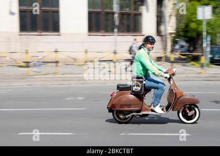 Belgrad, Serbien - 24. April 2020: Reifer Mann im Retro-Outfit, der an einem sonnigen Tag auf der leeren Straße in Dorcol auf dem Oldtimer-Roller vespa unterwegs ist Stockfoto