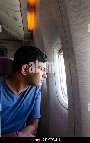 Nahaufnahme eines erwachsenen Mannes, der aus einem Flugzeugfenster mit einem angespannten Blick ins Gesicht schaut. Stockfoto