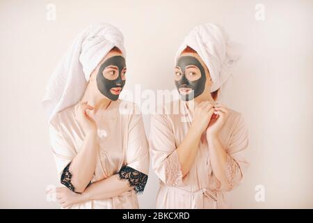Zwei junge Schwestern in Bademänteln mit Handtüchern auf dem Kopf isoliert auf weißem Hintergrund. Spa zu Hause. Sie machen eine Maske für die Hautpflege auf der Stockfoto