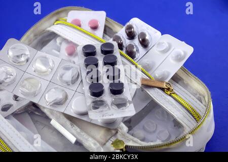 Weiße offene Handtasche mit halbleeren Blisterpackungen aus rosa, weißen und braunen Tabletten auf blauem Hintergrund, Stockfoto