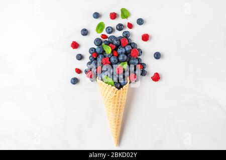 Frische Sommerbluebeeren und Himbeeren mit Minze in Waffelkegel auf weißem Marmorgrund. Sommer Food Konzept. Flache Lage. Draufsicht mit Kopierraum. Stockfoto