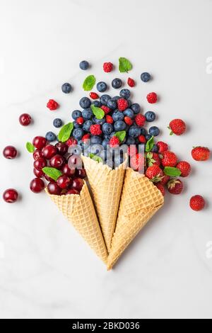 Heidelbeeren, Himbeeren, Erdbeeren und Kirschenbeeren in Waffeleiszapfen auf weißem Marmortisch. Flacher Lay. Draufsicht. Sommer Food Konzept. ve Stockfoto