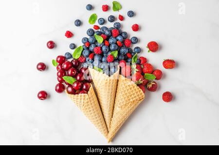 Frische Sommerbeeren mit Minze in Waffel-Eis-Zapfen auf weißem Marmor Hintergrund. Sommer Food Konzept. Flach legen. Draufsicht mit Kopierraum. Stockfoto