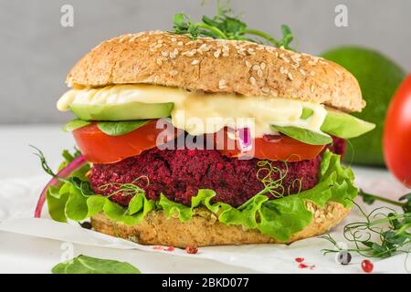 Veganer Rote Bete Burger mit Avocado, Salat, Tomaten, Sprossen und veganer Mayonnaise auf weißem Marmortisch. Gesundes Fast Food Stockfoto