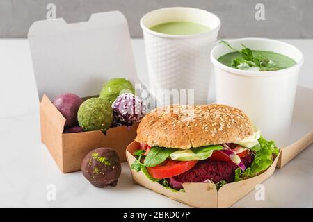 Lieferung von Lebensmitteln. Vegane Rübenburger und Energiebällchen in Öko-Pappkartons mit Erbsensuppe und Matcha Latte in Einwegbechern. Gesunde Ernährung Mittagessen zu ta Stockfoto