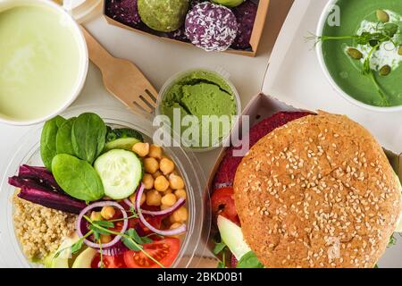 Gesunde vegane Lebensmittel liefern. Buddha Schüssel Salat, Burger, Suppe, Dessert und Matcha Latte in Kisten und Tassen verpackt. Draufsicht. Flaches Lay. Restaurant-Menü en Stockfoto