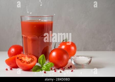 Tomatensaft im Glas mit Salz, frischen Tomaten, Basilikum und Pfeffer auf weißem Marmortisch Stockfoto