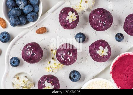 Rohe vegane Energiebeiße oder Bälle aus Heidelbeere, acai, Nüssen und Datteln mit Blumen serviert. Draufsicht. Styling für Speisen. Gesundes Dessert Stockfoto