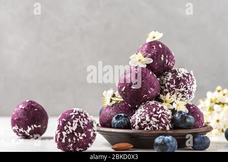 Rohes veganes Essen Dessert. Heidelbeer-Energiebällchen oder Bisse aus frischen Beeren, Nüssen und Datteln mit Blumen serviert. Styling für Speisen Stockfoto