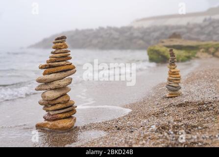 Steinpyramide auf Sand symbolisiert Zen, Harmonie, Gleichgewicht. Positive Energie. Ozean im Hintergrund Stockfoto