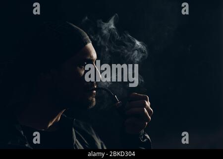 Mann, der eine Pfeife auf dunklem Hintergrund raucht. Profilhochformat. Stockfoto