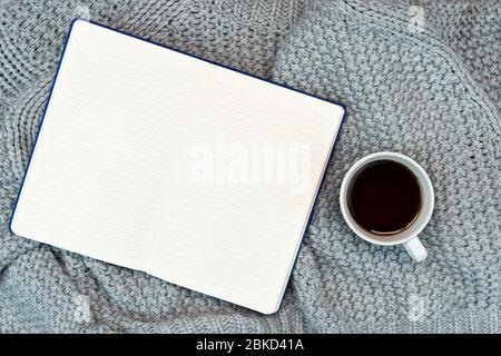 Gemütlicher Schreibplatz mit warmem Pullover, Kaffee, Laptop und Schreibzubehör. Arbeiten Sie von zu Hause aus. Schreiben. Warmes Konzept bei kaltem Wetter. Stockfoto