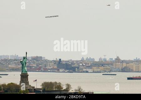 New York, New York, USA. Mai 2020. Ein kleines Flugzeug fliegt mit der Nachricht #capitalisthepandemie über New York City und stellt seine Botschaft an New Yorker aus, die draußen das warme Wetter genossen. Das Flugzeug hier wird von der Freiheitsstatue im NY Harbour geflogen. Quelle: Jodi Jones/ZUMA Wire/Alamy Live News Stockfoto