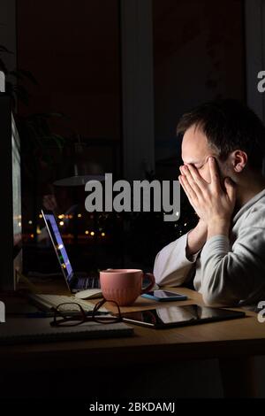 Müde Freelancer Mann reibt sich die Augen, sitzt an einem Desktop-PC / Laptop spät in der Nacht, schläft aus Müdigkeit. Stockfoto