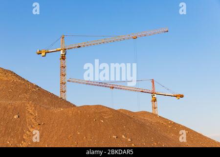 Hoher Sandhaufen und Gruppe Hochhaus-Turmkrane auf der Baustelle, Sonnenuntergang Himmel Hintergrund. Zukünftiger Wohnkomplex. Stockfoto