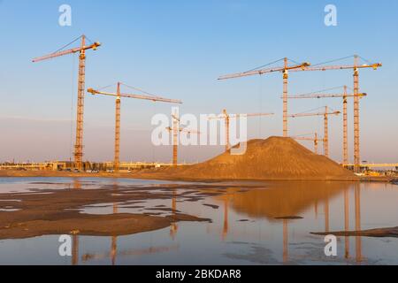 Hoher Stapel von Sand und Gruppe Hochhöhe Turmkrane auf Baustelle, Sonnenuntergang Himmel Hintergrund.Zukunft Wohnanlage. Stockfoto