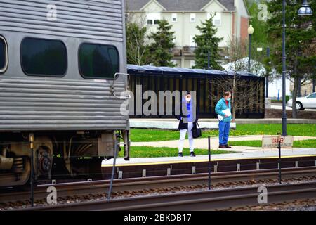 Winfield, Illinois, USA. Passagiere mit Gesichtsmasken warten auf die Ankunft eines Metra-Pendlerzuges am Bahnhof. Stockfoto