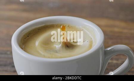 Nahaufnahme in einer Tasse duftenden Espresso mit Schaum fallen Kaffee Spritzer auf einem braunen Holztisch. Zeitlupe, Full HD-Video, 240 Bilder/s, 1080p. Stockfoto