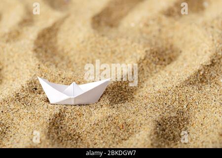 Weißes Papierboot auf gelbem welligen Sand. Das Konzept der Trockenheit, Wüstenbildung, der Verwacknung von Flüssen und Seen. Nachteilige Klimaänderungen. Umwelt Stockfoto