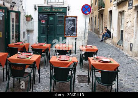 Restaurant im Freien in den Straßen von Alfama mit einem Mann im Hintergrund mit dem Handy, Lissabon, Portugal Stockfoto