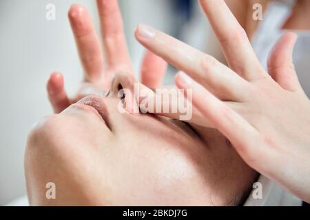 Gesichtsmassage. Finger des Masseurs. Nase und Hände in Nahaufnahme. Gesichtspflege. Frau im Schönheitssalon. Stockfoto
