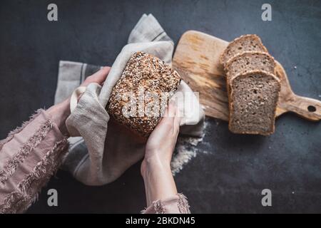 Die Hände der Frau halten einen Laib Buchweizenbrot mit Sonnenblumenkernen. Stockfoto