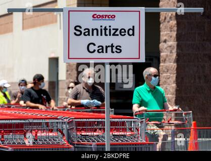 COVID-19 Pandemie zwingt zu Veränderungen im Shopping: Ein Schild weist Käufer zu desinfizierten Karren, und Käufer mit Gesichtsmasken warten, um den Laden zu betreten. Stockfoto