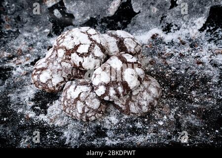 Frisch gebackene süße Schokoladenkekse am Backblech. Kekse mit Puderzucker auf einem strukturierten Hintergrund bestreut. Hausmannskost Stockfoto