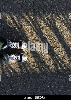 Canvas Sneaker Schuhe auf den Füßen der Frau auf dem Asphalt mit Schattenlinien. Stockfoto