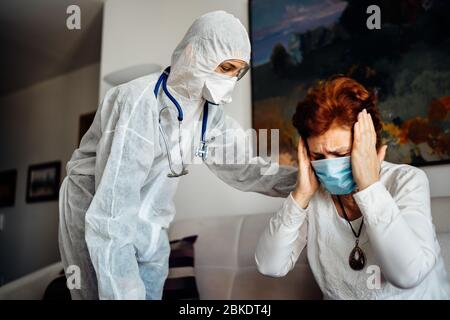 Coronavirus Frontlinie Arzt zu Hause Behandlung von Senior COVID-19 kranken Patienten.Patient zu Hause Pflege Besuch.Healthcare Arbeiter in PSA-Hazmat Anzug Tests.Home c Stockfoto