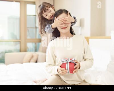 Happy Little Asian Girl Mutter ein Geschenk und bedeckt Mutter die Augen mit Händen Stockfoto