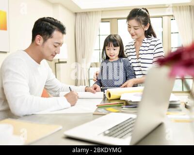 Junge asiatische Mutter und Tochter beobachten Vater Zeichnung ein Design während der Arbeit von zu Hause (Kunstwerk im Hintergrund digital verändert) Stockfoto