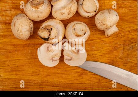 Hälften von geschnittenen Pilzen und jungen Pilzen auf einem hölzernen Hintergrund verstreut. Nahaufnahme Stockfoto