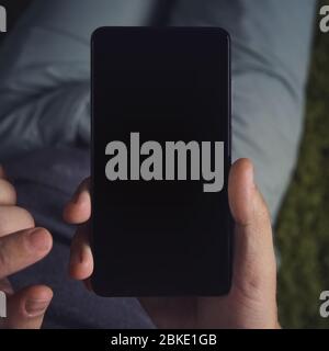 Nahaufnahme eines jungen Mannes, der lang hält Smartphone mit dem schwarzen Bildschirm. Person ist online von einem Smartphone. Mann berührt das schwarze Handy sc Stockfoto
