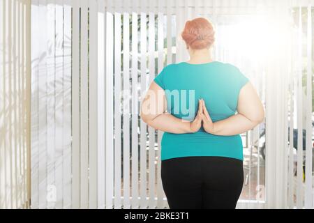 Stehend plus size Frau tun Reverse Gebet Pose, um ihre Arme zu stärken, Blick von hinten Stockfoto