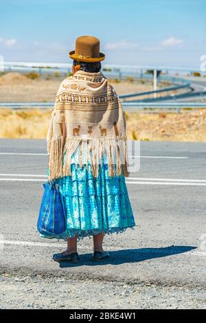 Bolivianische indigene Aymara Frau wartet auf den Transport entlang der Autobahn in traditioneller Kleidung, La Paz, Bolivien. Stockfoto