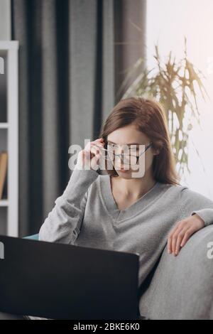 Ernste dunkelhaarige Frau, die Laptop für die Arbeit an der Fernbedienung verwendet Stockfoto